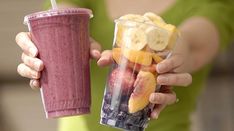 a person holding up a smoothie with fruit in it and a drink to go