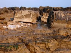 there is a large pipe sticking out of the water near some rocks and debris on the beach