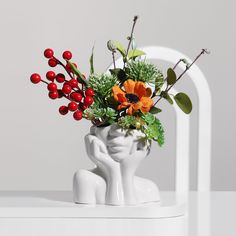 a vase filled with flowers and greenery on top of a white table