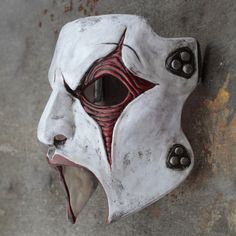 a white mask with red and black details on it's face hanging from a wall