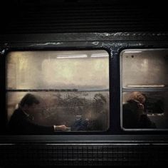 two people sitting on a train looking out the window at something in the distance,