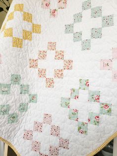 a white quilt with yellow and pink squares on the top, sitting on a table