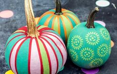 three painted pumpkins sitting next to each other on top of a black surface with confetti around them