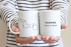 two people holding coffee mugs with the words always close at heart and map on them