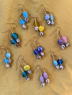 a collection of earrings with different designs and colors on them sitting on a cloth covered surface