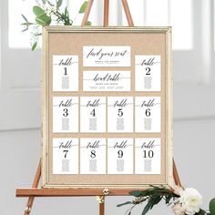 a wooden easer with seating cards on it and flowers in the vase next to it