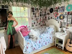 a woman standing next to a bed in a room with pictures on the walls and floor