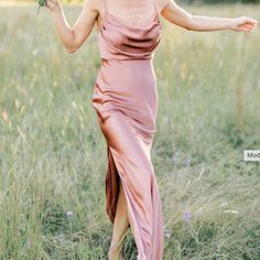 a woman in a pink dress is walking through the grass with her arms spread out