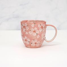 a pink coffee cup with flowers painted on the outside and inside, sitting on a white surface