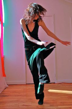 a woman in black shirt and green pants doing a dance move on wooden flooring