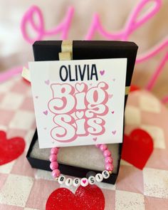 a pink and white bracelet with black letters on it sitting in front of a box