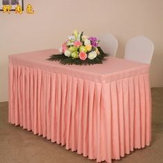 the table is covered with a pink cloth and flowers on it, along with two white chairs