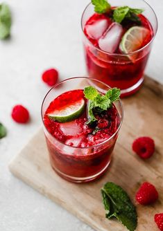 two glasses filled with raspberry mojitas on top of a cutting board