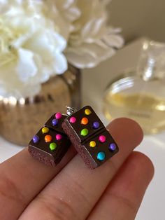 a hand holding two small chocolate pieces with multicolored candy toppings on them