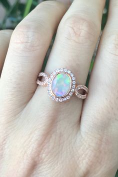 "An Oval Faceted Natural and Genuine Opal set in a bezel setting accented with petite white sapphires handcrafted in your choice of 10k/14k/18k Rose/Yellow Gold or White Gold. This ring makes a lovely engagement/promise/October birthstone/statement ring. Wrapped in a Box ready for gift giving.(r-egt-20) Please note each opal has a unique play of color, if you wish for a certain color in the fire, please let us know and we will try to accommodate your request. View our Instagram video of this Rin Oval Opal Promise Ring With Accent Stones, Oval Opal Rings With Bezel Setting, Oval Cabochon Opal Ring With Accent Stones For Anniversary, Oval Rose Gold Opal Gemstone Ring, Cubic Zirconia Opal Promise Ring, Oval Shape, Rose Gold Oval Opal Gemstone Ring, Oval Opal Jewelry With Bezel Setting, Rose Gold Oval Opal Ring, Rose Gold Oval Opal Promise Ring