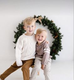 two young boys sitting on top of each other in front of a wreath