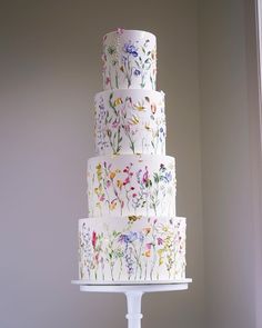 a three tiered cake with flowers painted on the side and white icing, sitting on a pedestal