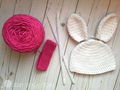 a crocheted bunny hat next to a ball of yarn and two knitting needles