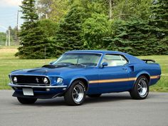 a blue muscle car parked in front of some trees