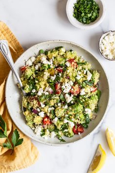 a white bowl filled with vegetables and feta cheese next to lemon wedges on a yellow napkin