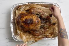 a person holding a roasting pan with a turkey in it and wrapped in foil