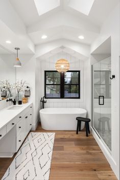 a bathroom with a white bathtub and wooden flooring next to a large window