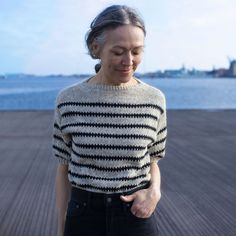 a woman standing on a pier looking down at her cell phone while wearing a black and white striped sweater