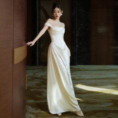 a woman in a long white dress leaning against a wall with her hand on the door