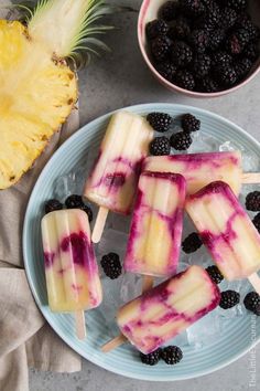 popsicles with blueberries and blackberries on a plate next to a pineapple