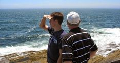 two men looking out at the ocean from a cliff