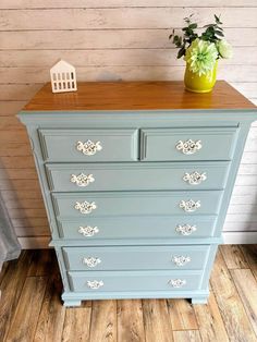 an old dresser painted in blue with white trim and gold hardware on the top, next to a potted plant