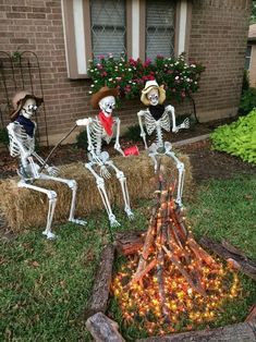 three skeletons sitting on hay bales in front of a house with flowers and pumpkins