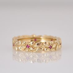 a yellow gold wedding band with pink sapphires and leaves in the center, on a reflective surface