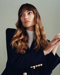 a woman with long hair wearing a black jacket and pearls on her collar, posing for the camera