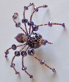 a purple and black spider made out of glass beads on a white surface with gold accents