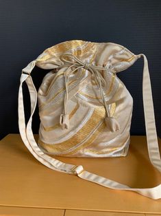 A bag remade of obi. An elegant shoulder bag made of gold, silver, and beige traditional wave patterned obi. The opening can be tied with a string. It shines in the light and creates a gorgeous look. The length of the handle is adjustable.  SIZE  height: 30 cm  width : 29 cm      depth: 8 cm  inner pocket: 17cm x 15 cm inner pocket with zipper: 18 cm x 18 cm handle: 60 cm ~ 108 cm It has a bottom plate. When ironing, be sure to apply a cloth.  NOTE  Since it is a remake work of a vintage obi, it Modern Gold Rectangular Bucket Bag, Modern Gold Bucket Bag For Formal Occasions, Elegant Gold Bucket Bag For Everyday Use, Elegant Gold Bucket Bag For Daily Use, Modern Gold Bucket Bag For Evening, Elegant Gold Bucket Bag For Everyday, Elegant Silver Bucket Bag, Modern Gold Evening Bucket Bag, Modern Gold Shoulder Bag As Gift