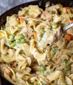 a spoon full of pasta with peas and chicken in it is being held over the skillet