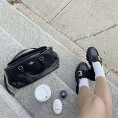 a woman's legs and purse sitting on the ground next to some coffee cups