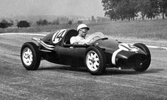 an old photo of a man driving a race car down the road in black and white