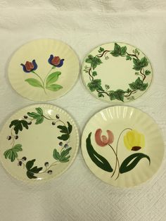 four plates with flowers painted on them sitting on a white tablecloth covered table cloth