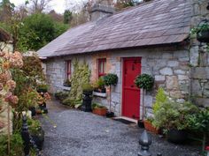 a stone house with potted plants in the front and red door on the side