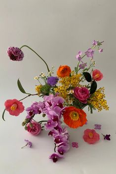 a vase filled with lots of flowers on top of a white table next to purple and orange flowers