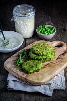 some food is laying out on a cutting board next to bowls of peas and yogurt