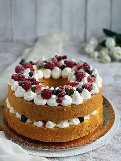 a cake with berries and whipped cream on top sitting on a plate next to flowers