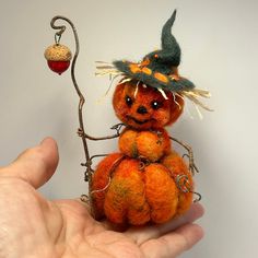 a hand holding a miniature orange pumpkin with a witch hat on it's head