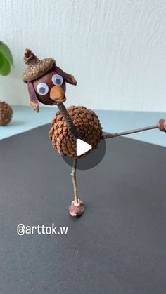 a pine cone bird with a hat on it's head is holding a stick