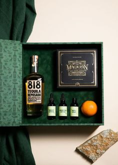 an open box containing three bottles of liquor and two oranges on a table next to a book