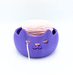 a purple cat shaped container with yarn in it's mouth and eyes on top