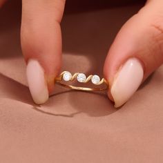 a woman's hand holding a gold ring with three diamonds on top of it