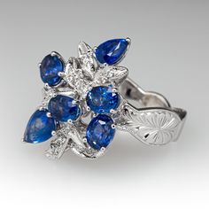 This captivating cluster style ring is accented with four (4), prong set, oval mixed cut natural sapphires and two (2), prong set, pear mixed cut natural sapphire. The sapphires are bordered with two (2), prong set, round brilliant cut diamonds and fourteen (14), bead set, round brilliant/single cut diamonds, bordered with milgrain edging. Engraved details accent the shoulders of the shank. The ring measures 22.6mm at the top, rises 9.8mm above the finger, tapering to 3.8mm wide and 1.3mm thick at the base of the shank. This ring is currently as size 6.5. Luxury Pear-shaped Sapphire Ring With Rose Cut Diamonds, Fine Jewelry Pear-shaped Sapphire Ring, Pear-shaped Multi-stone Sapphire Ring For Anniversary, Marquise Sapphire Ring With Rose Cut Diamonds, Elegant Pear-shaped Multi-stone Sapphire Ring, Cluster Sapphire Ring In Fine Jewelry Style, Pear-shaped Sapphire Multi-stone Ring, Blue Sapphire Diamond, Bead Set